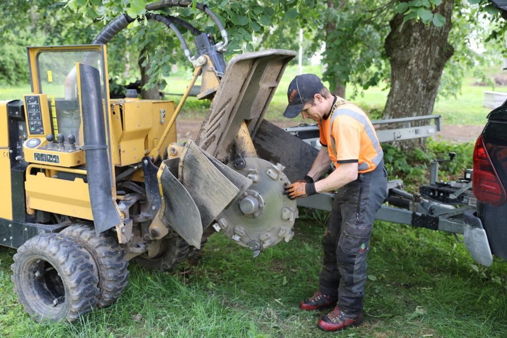 Mies korjaa puunkannon jyrsintään tarkoitettua konetta. Hän kiinnittää uutta terää pyöreään sahaan.