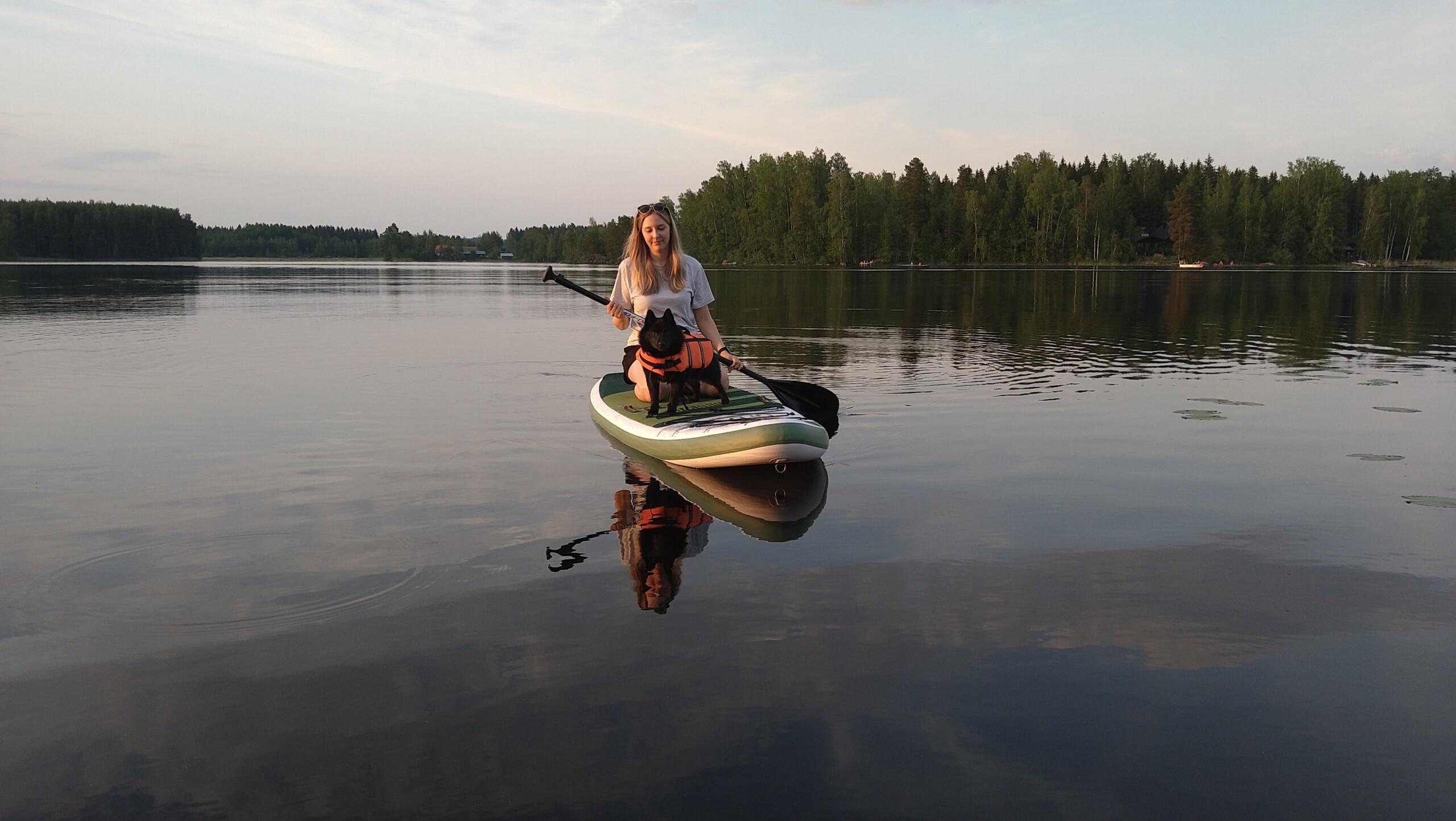 Nainen ja pieni koira sup-laudan päällä järvellä.