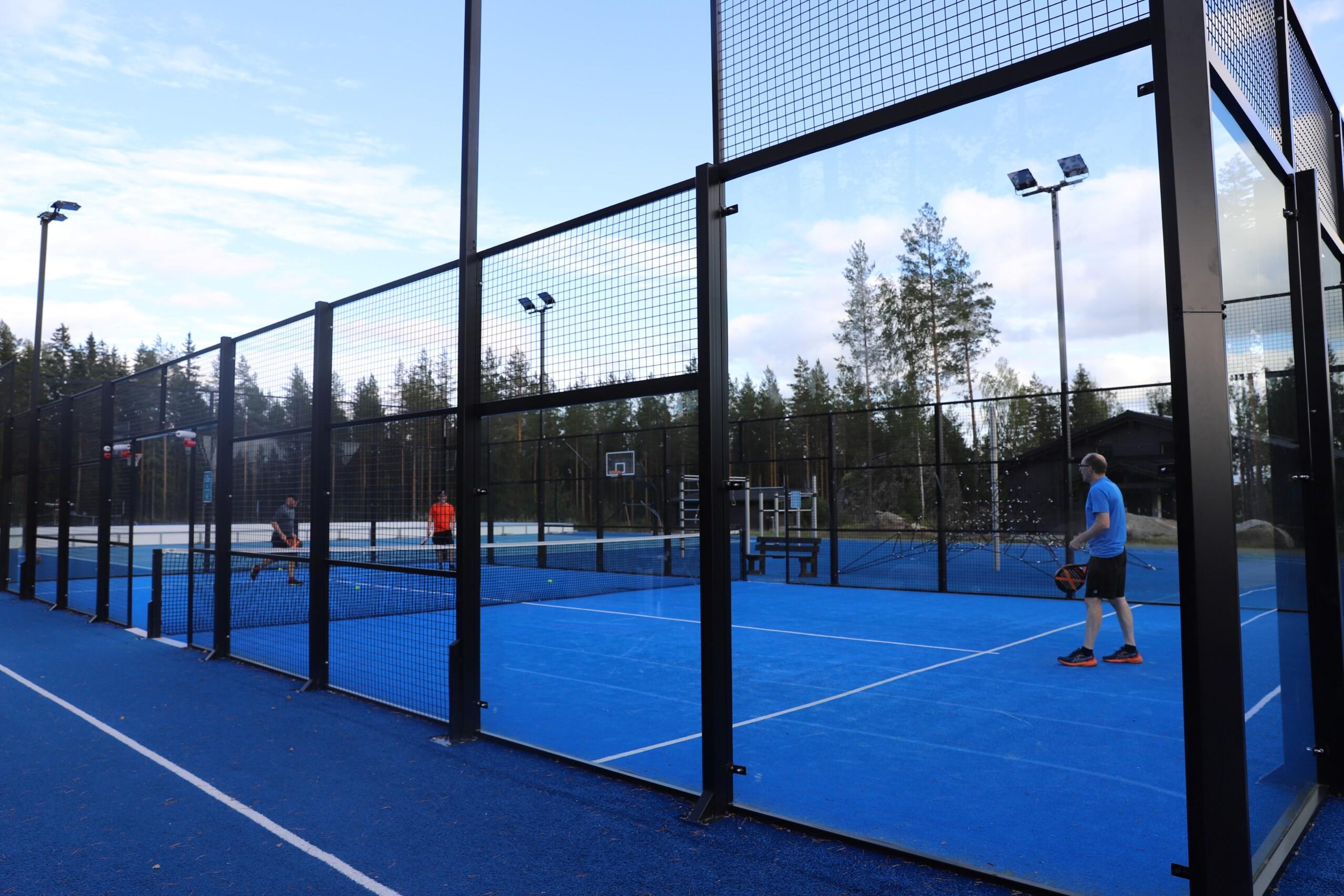 Padelkenttä. Kolme miestä kentällä mailojen kanssa.