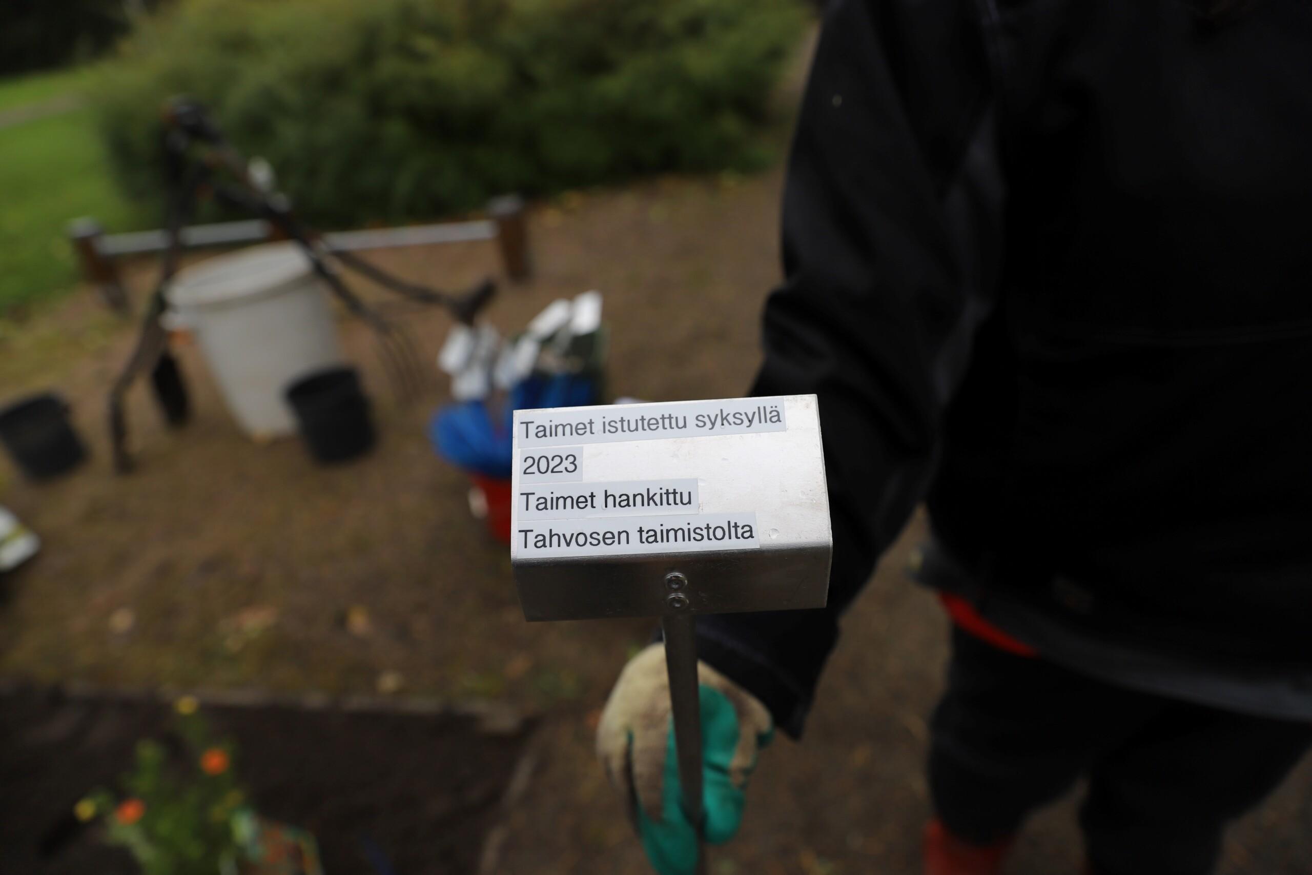 Käsi pitelee varrellista nimikylttiä.