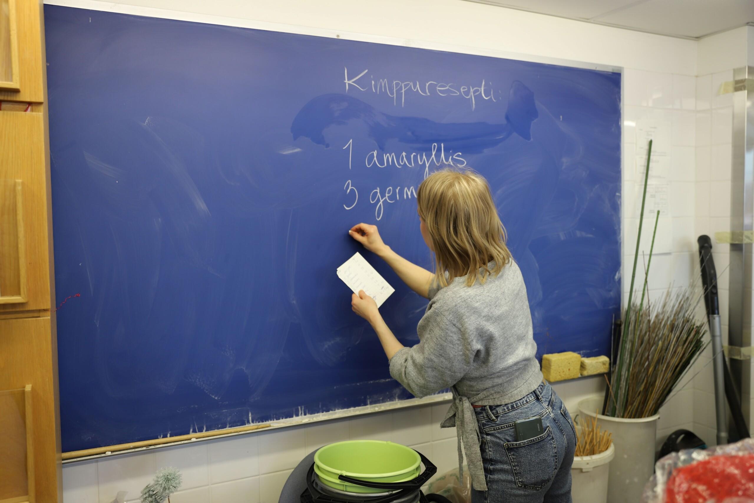 Nainen kirjoittaa liitutaululle lapulta kimppureseptiä.