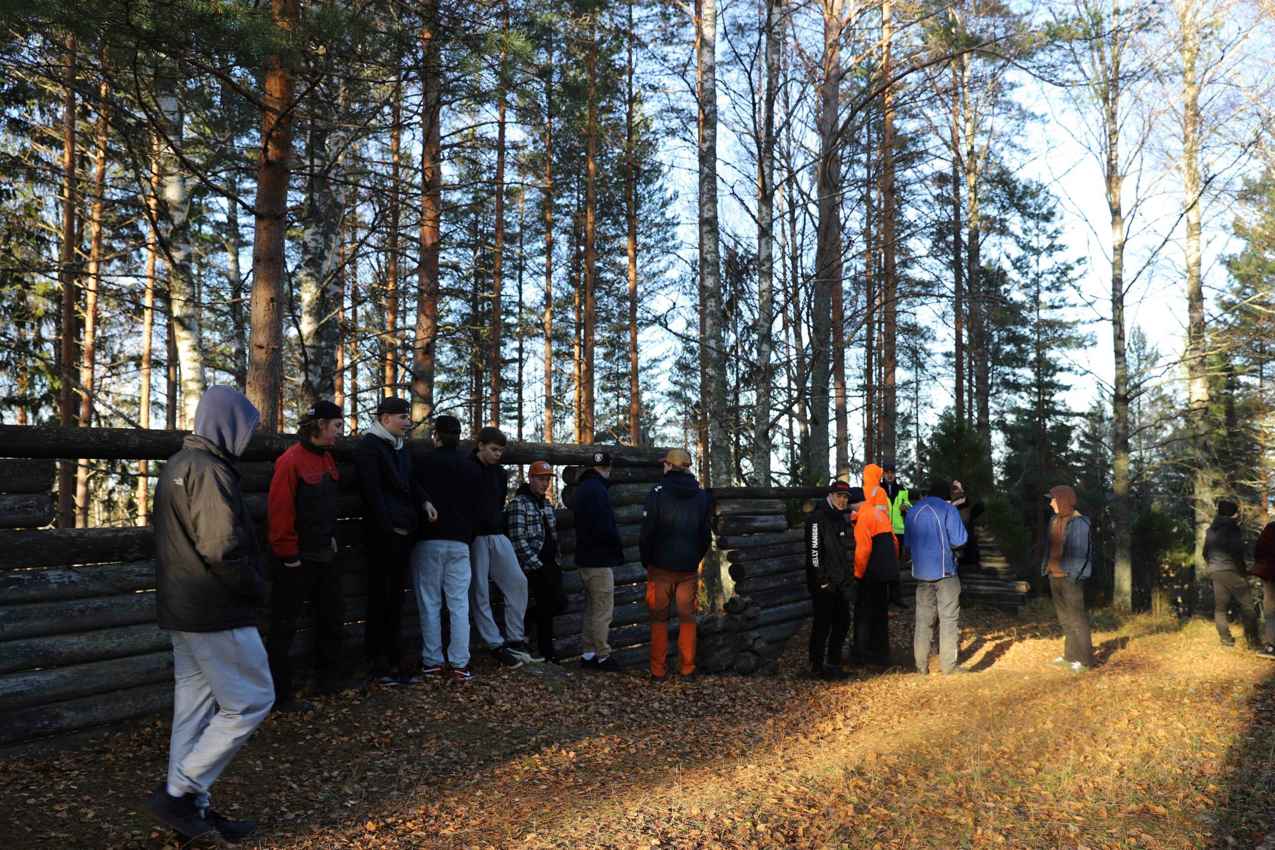 Joukko nuoria seisoo luonnossa vanhan puulinnoituksen edessä.