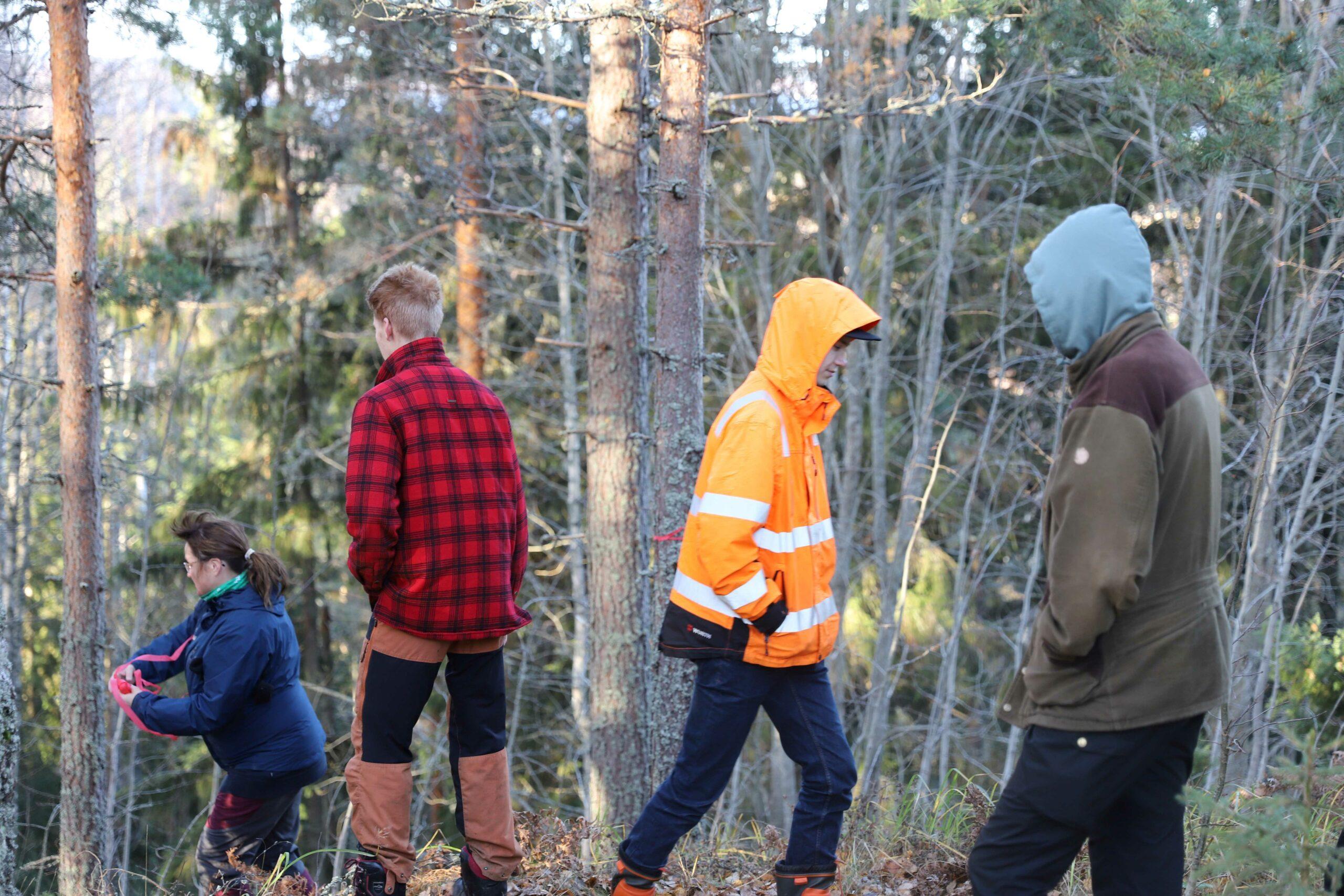 Nainen kävelee rinnetta alas nauharulla kädessä. Kaksi nuorta miestä katsoo hänen peräänsä. Yksi nuori mies kävelee naisesta pois päin.