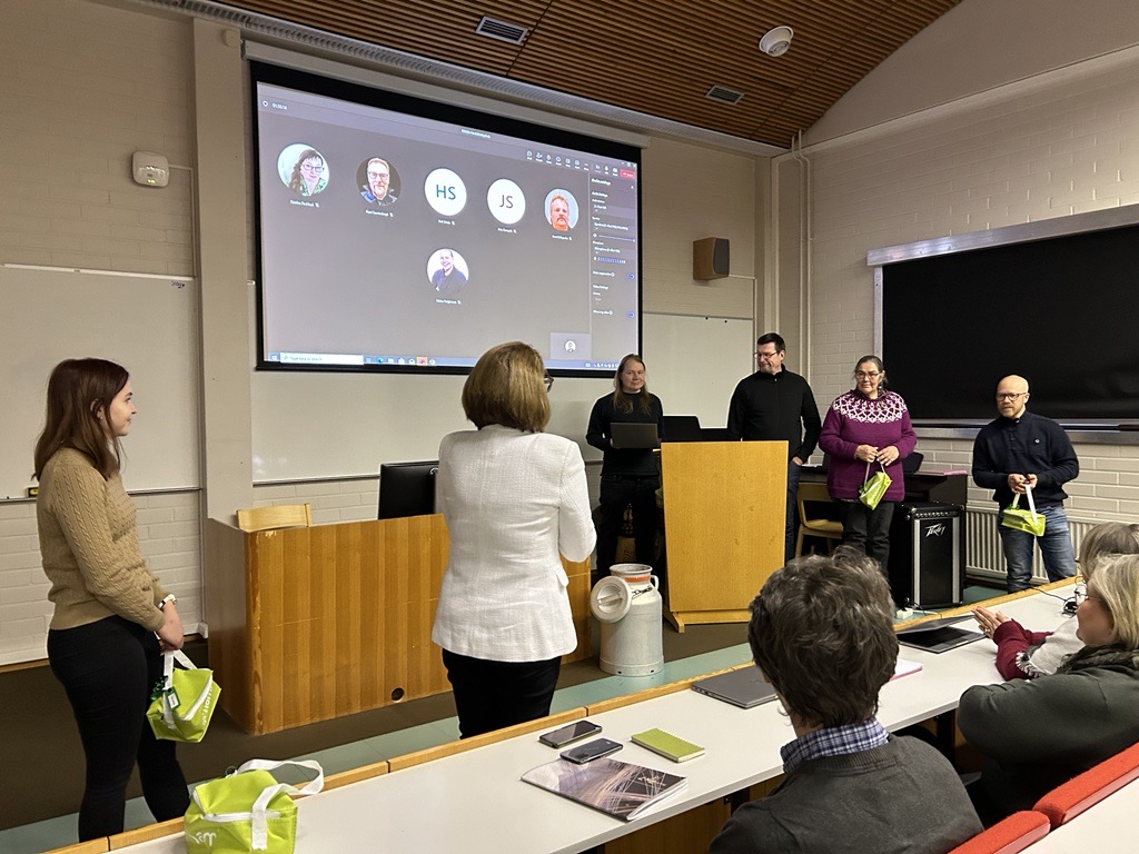 Joukko ihmisiä seisoo auditorion edessä.