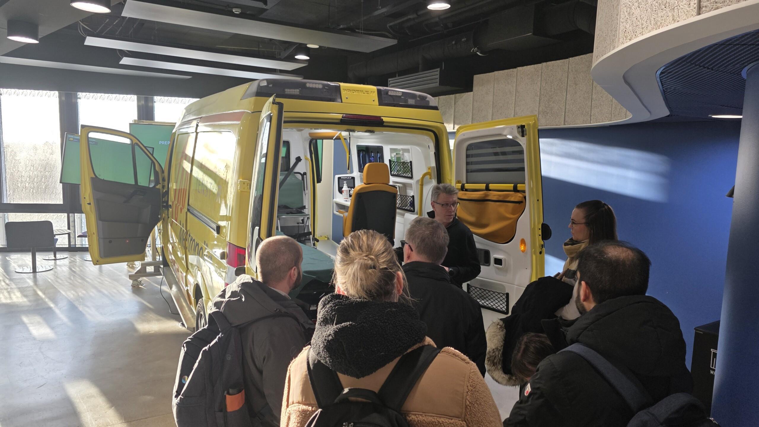 kuusi ihmistä on ambulanssisimulaattorin vieressä