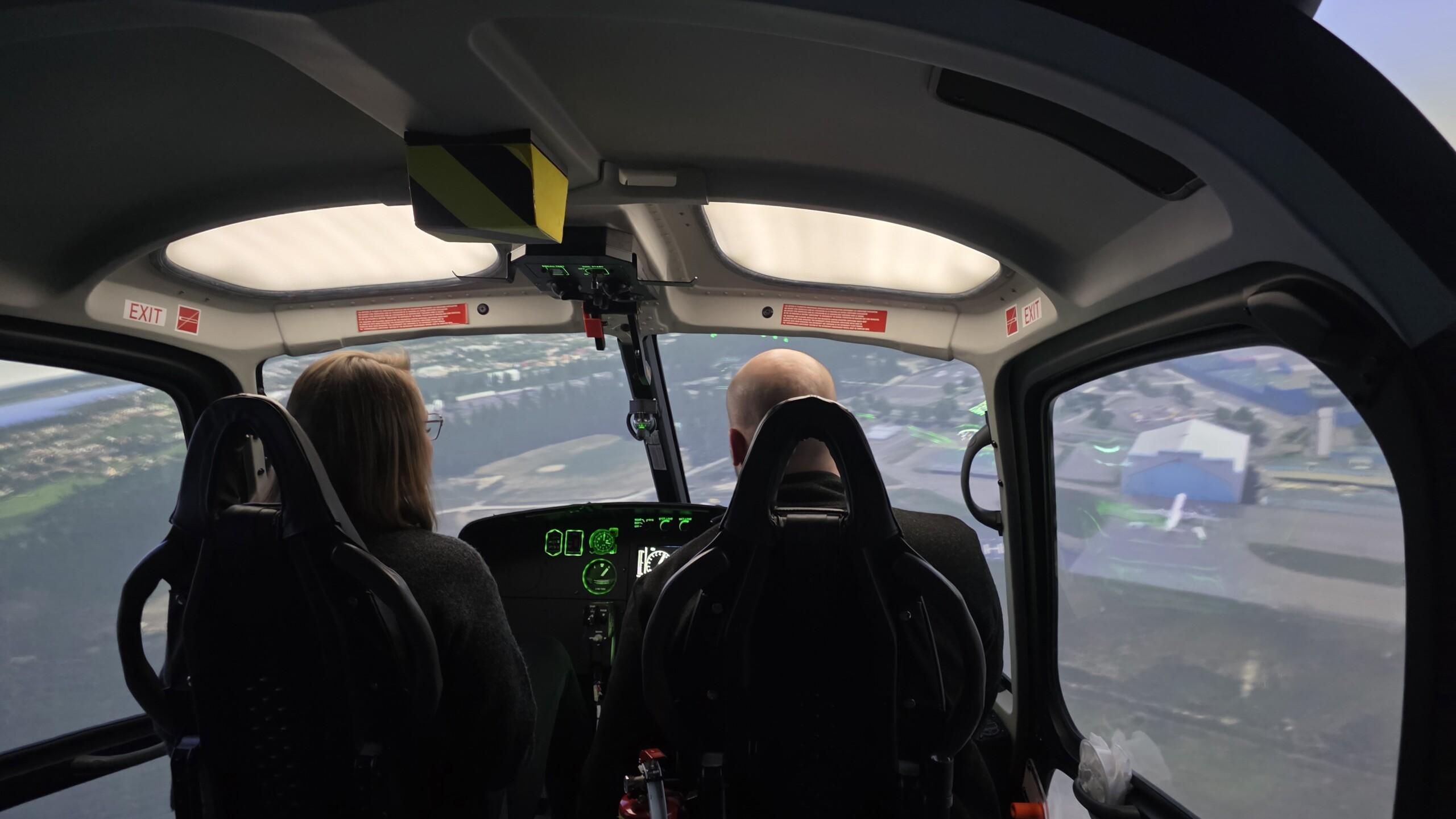 Kaksi henkilöä, mies ja nainen käyttävät helikopterisimullaattoria. 