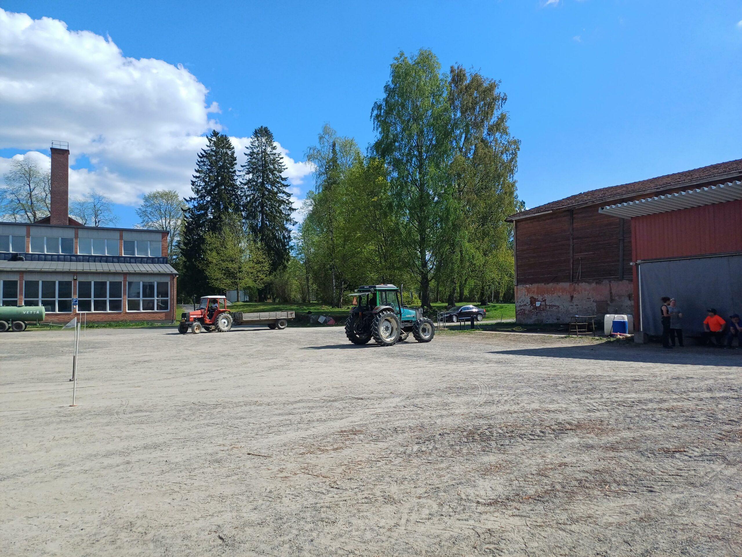 Suuri hiekkainen sisäpiha. Traktori. Traktorihalleja.